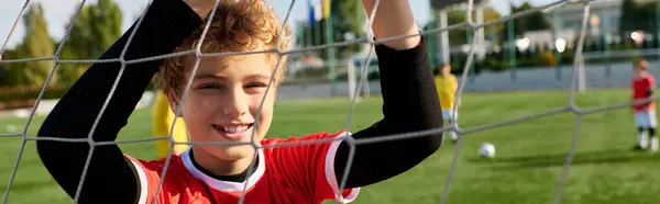 決意を持った少年は サッカーの網の後ろに立っている 彼は彼のゴールキーピングスキルを実践しています 敏捷性と精度で目標を守る準備ができています — ストック写真