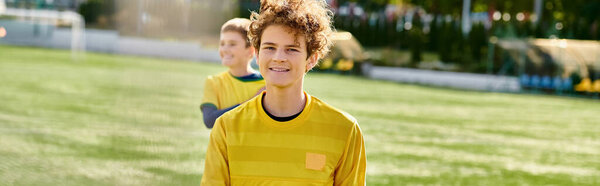 A young man exudes a sense of triumph as he stands atop a vast, vibrant green field, surrounded by lush vegetation under a clear blue sky.