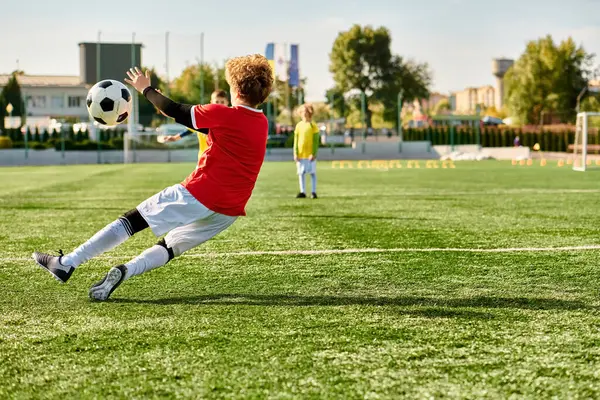stock image A young boy energetically kicks a soccer ball, sending it soaring across a vast field. His focused expression and precise technique demonstrate his passion for the sport.