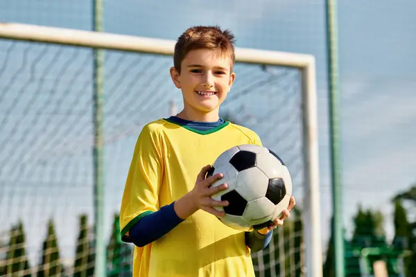stock image A young boy, determined and focused, holds a soccer ball in front of a goal, ready to take a shot with precision and skill.