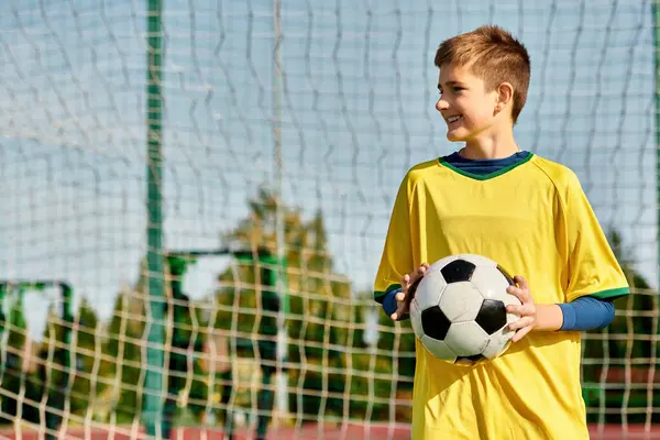 一个小男孩自信地站在球门前 手里拿着足球 憧憬着自己的胜利 他凝视着网 眼神坚定 — 图库照片