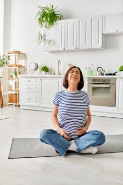 Olgun bir kadın, rahat mutfağındaki paspasla yoga yapıyor..