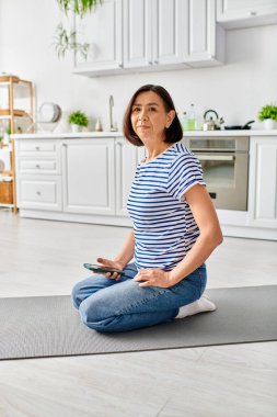 Rahat ev kıyafetleri içinde olgun bir kadın mutfağındaki bir paspasın üzerinde yoga yapıyor..