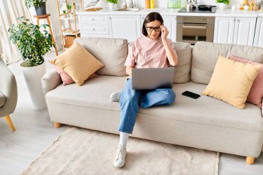 A mature woman in cozy homewear sits on a couch, focused on her laptop screen. clipart