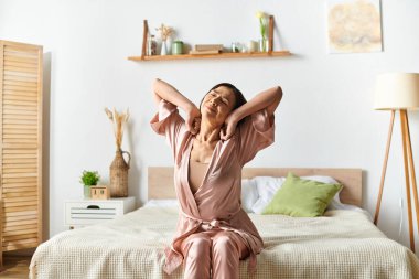 Woman joyful and free on a bed, arms raised in celebration. clipart