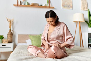 Pembe pijamalı olgun bir kadın rahat bir şekilde yatakta oturur..