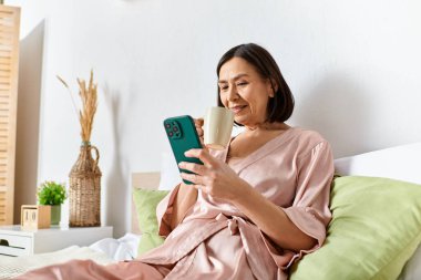Rahat bir ev elbisesi içinde bir yatakta oturan, cep telefonuna dalmış bir kadın..