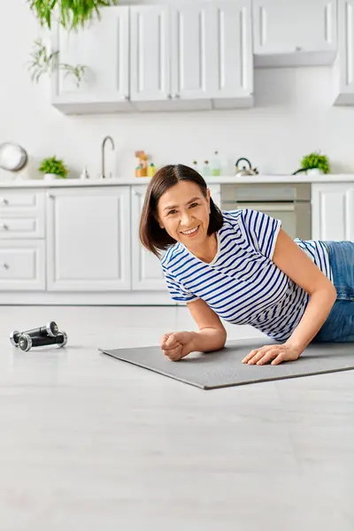 一位穿着家居服的成熟女子在阳光充足的厨房的垫子上练习瑜伽 — 图库照片