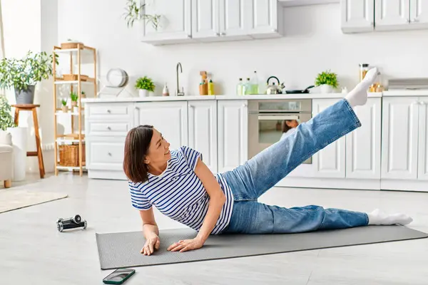 stock image Mature woman in cozy homewear doing yoga on a kitchen mat.
