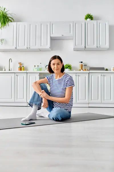 穿着舒适家居的成熟女人在厨房的垫子上练习瑜伽 — 图库照片