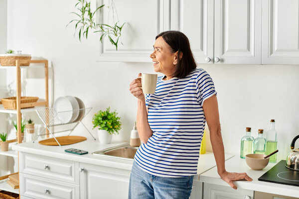 A mature woman enjoys a serene moment in her kitchen, holding a cup of coffee.