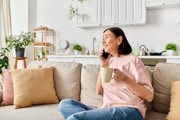 A mature woman in cozy homewear enjoying a cup of coffee while sitting on a couch.