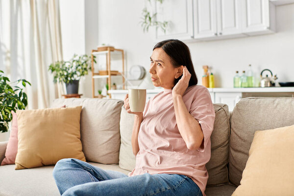 Relaxing woman in homewear sits on couch, savoring coffee.