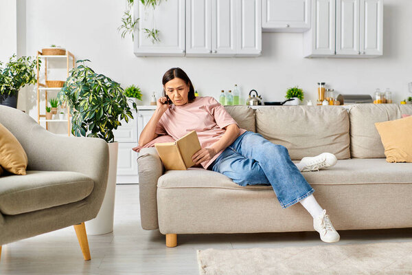 A woman in cozy homewear sitting on a couch, engrossed in reading book.