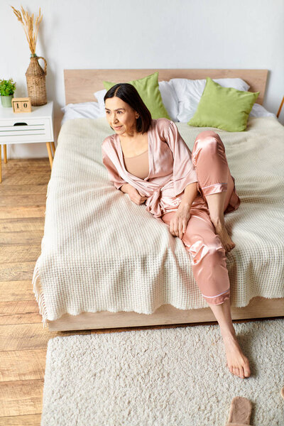 A woman in cozy homewear sits on a bed in a bedroom.