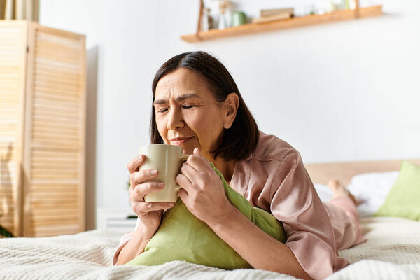 A woman in cozy homewear sitting on a bed, holding a cup of coffee.