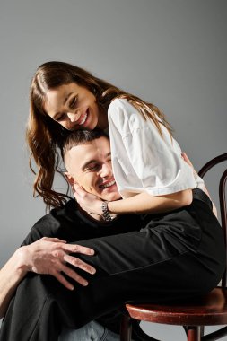 A woman gracefully sitting on top of a man on a chair, depicting connection and balance between a young couple in love. clipart
