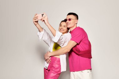 A stylish young couple in love takes a selfie together in a studio with a grey background. clipart