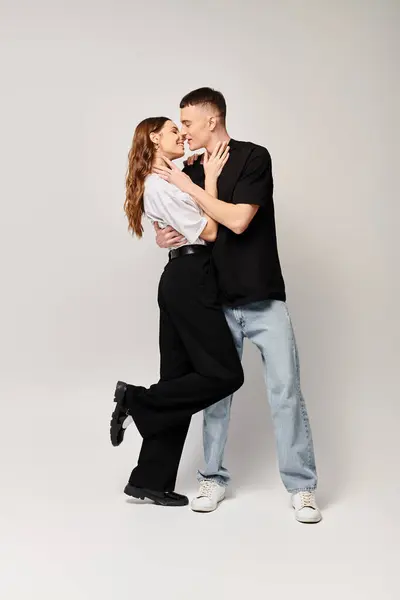 stock image A man and a woman, young couple, dancing together in a studio with a grey background, showing love and harmony.