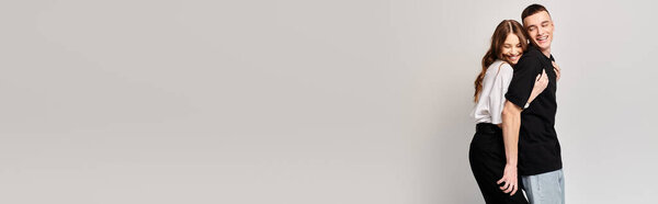 Молодой человек и женщина стоят бок о бок в студии, демонстрируя свою любовь и связь перед серым фоном.