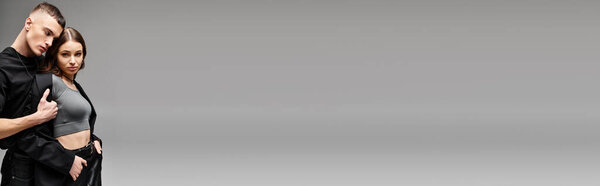 Молодой человек и женщина стоят бок о бок, излучая любовь и единение в студии с серым фоном.