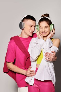 Tarz sahibi genç bir çift birlikte müzik dinliyorlar, kulaklık takıyorlar gri bir stüdyonun arka planına karşı.