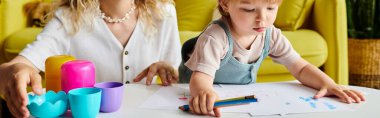 A curly-haired mother and her toddler daughter sit at a table, engaging in Montessori learning activities in a cozy home setting. clipart