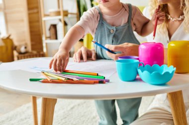 Kıvırcık bir anne ve küçük kızı bir masada Montessori öğrenme aktivitelerine dalmış durumdalar..