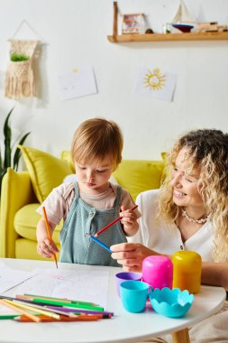 Kıvırcık bir anne ve küçük kızı öğrenme ve keşfetme dünyasına dalmış bir masada Montessori eğitimine giriyorlar..