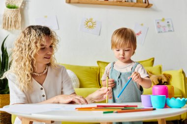 Kıvırcık saçlı bir kadın ve yürümeye yeni başlayan kızı bir masada birlikte Montessori eğitim faaliyetlerinde bulunuyorlar..