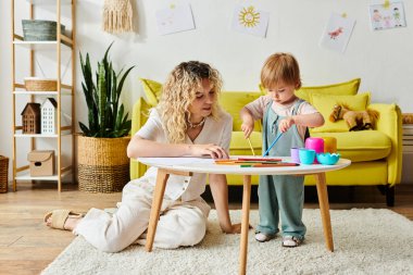 Kıvırcık bir anne ve küçük kızı evdeki Montessori oyuncaklarını kullanarak oyun oynuyorlar, merakı ve öğrenmeyi teşvik ediyorlar..