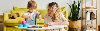 Kıvırcık saçlı bir anne, evde Montessori eğitim yöntemlerini uygulayan küçük kızıyla bir masada etkin bir şekilde takılıyor..