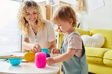 Kıvırcık saçlı bir anne ve küçük kızı evde eğitici Montessori oyuncaklarıyla oynuyorlar..