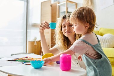 Kıvırcık bir anne ve küçük kızı evde renkli bardaklarla eğlenceli bir keşfe girişiyor, Montessori metodunu benimsiyor..