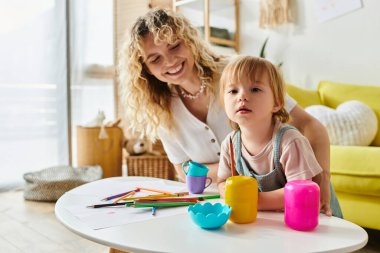 Kıvırcık saçlı bir anne ve küçük kızı renkli oyuncaklarla evde Montessori tabanlı oyun oynuyorlar..