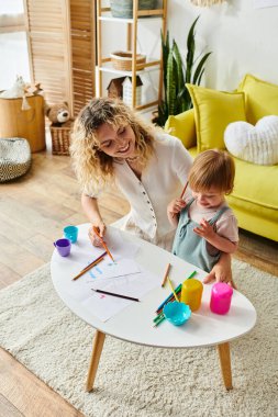 A curly-haired mother and her toddler daughter engage in Montessori learning in their warm and inviting living room. clipart