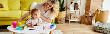 Kıvırcık saçlı bir anne ve yeni yürümeye başlayan kızı evde bir masada Montessori öğreniyorlardı..