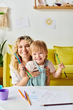 Kıvırcık saçlı anne ve küçük kızı evde Montessori öğrenme aktivitelerine odaklanmış bir masada oturuyorlar..