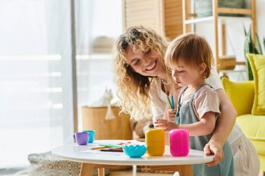 Kıvırcık saçlı bir anne ve küçük kızı evde Montessori 'den esinlenilmiş bir etkinlikte fincanlar kullanırken eğlenceli bir şekilde keşfettiler ve öğrendiler..