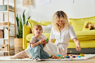 Kıvırcık anne ve küçük kızı evde, yerde oturmuş, eğlenceli Montessori metodu eğitimine girişiyor..