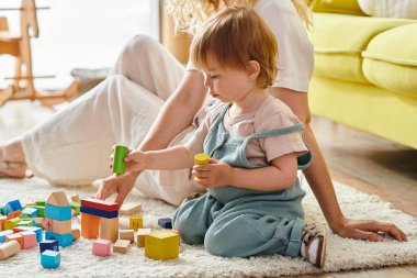 Kıvırcık bir anne ve yeni yürümeye başlayan kızı, Montessori yöntemini kullanarak yerde taş bırakarak öğreniyorlar..