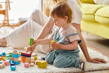 A curly mother and her toddler daughter engage in hands-on learning with blocks on the floor, using the Montessori method. clipart