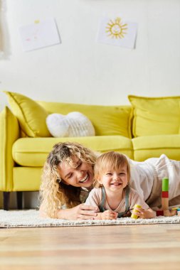 Kıvırcık bir anne ve küçük kızı evde Montessori eğitim yöntemini uygularken kucaklaşıyorlar..