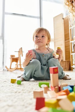 Küçük kız yerde oturuyor, renkli bloklarla dolu binaya dalmış, Montessori metodunu somutlaştırıyor..
