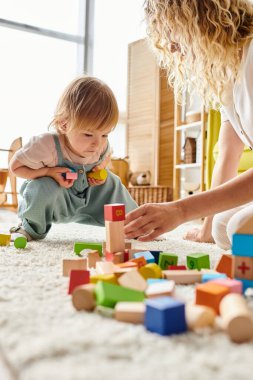 Kıvırcık bir anne ve küçük kızı yerde Montessori metodunu kullanarak eğitici bir oyun oynuyorlar..