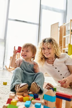 A curly-haired mother and her toddler daughter engage in educational play with blocks on the floor. clipart