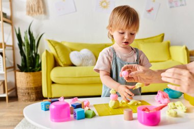 A curly-haired mother engages in the Montessori method with her toddler daughter, playing and learning together in a cozy living room. clipart