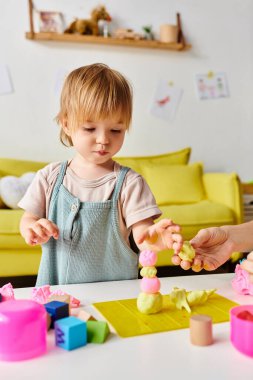 Anne, küçük kızının oyuncaklarla dolu bir masada Montessori 'de oynamasını izliyor..