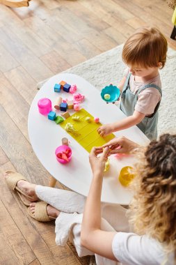 Kıvırcık bir anne ve küçük kızı Montessori eğitim metodunu kullanarak bir masada oyuncaklarla oynuyorlar..