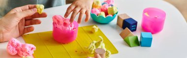 mother observes as her toddler daughter intricately molds and shapes colorful play dough on a table. clipart